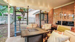 An outdoor patio area with a table and chairs, a brick wall, and a window with framed pictures. - The TX Oasis.  Boho Paradise.  Huge Backyard. (San Antonio)