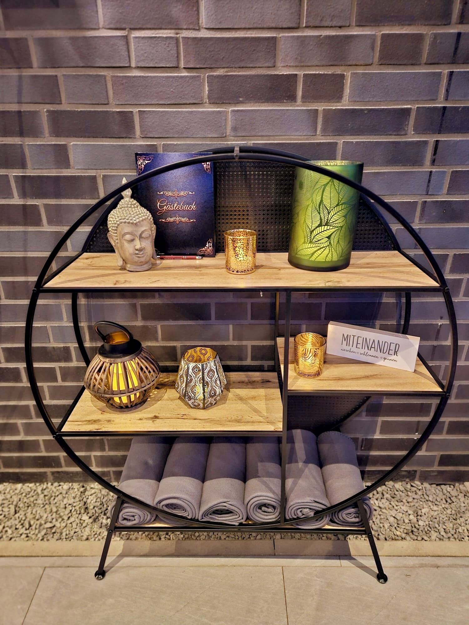 A display shelf with various decorative items including a Buddha head, a box labeled 'Gästebuch', and a green vase with leaf patterns.