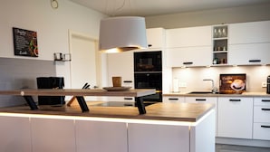 Une cuisine moderne avec des meubles blancs, un îlot central en bois et un luminaire suspendu.