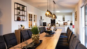 Un espace de salle à manger moderne avec une longue table en bois, des chaises noires et des lampes suspendues.