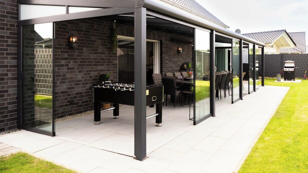 Un espace patio moderne avec des murs en verre, une table de baby-foot et des sièges d’extérieur.
