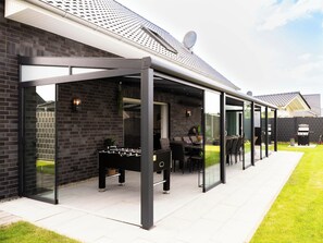 Een modern terras met glazen wanden, een tafelvoetbaltafel en buitenmeubels.
