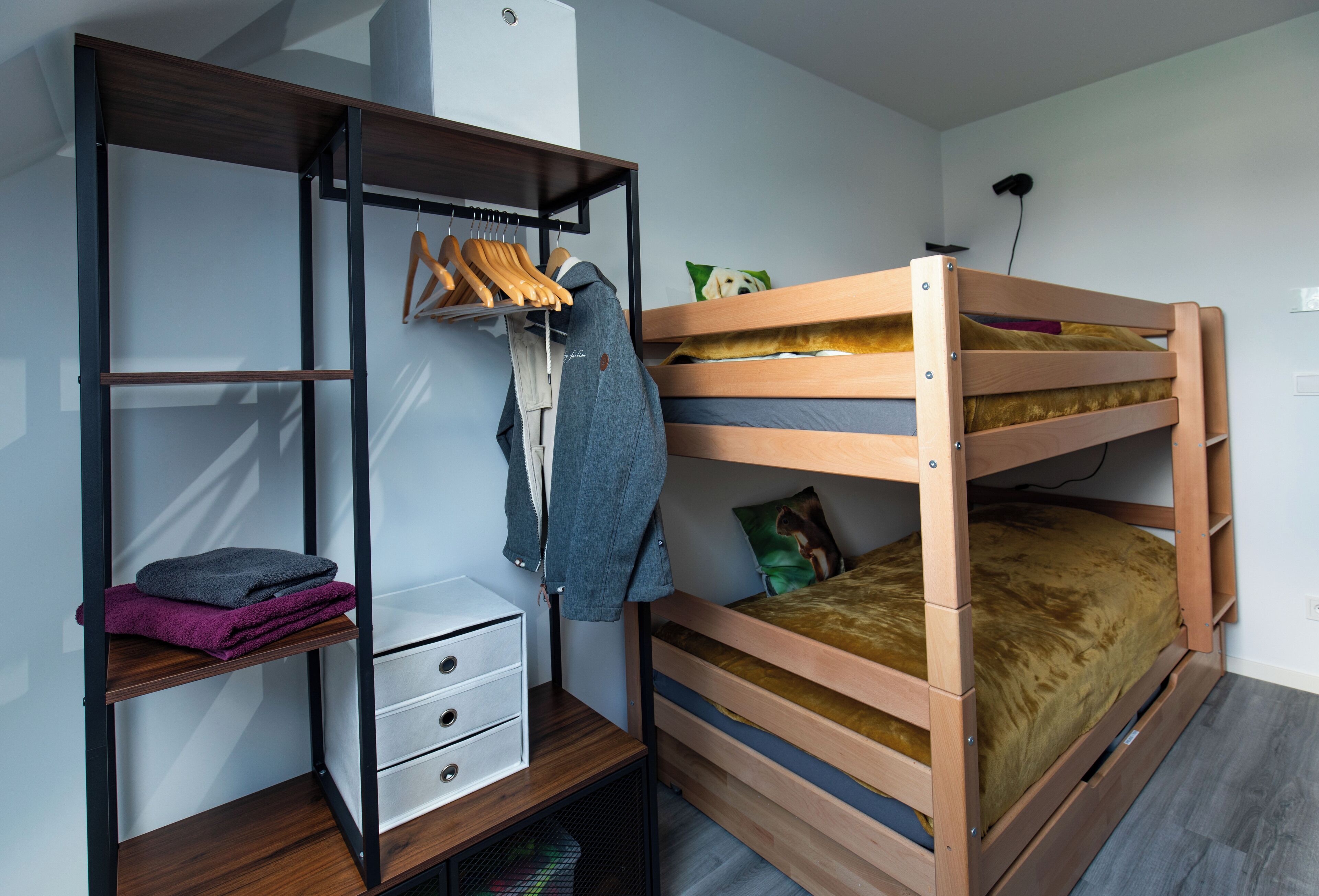 A bunk bed with a wooden frame, a wardrobe with open shelves, and a small desk with drawers.