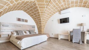 Ein Schlafzimmer mit Steindecke, einem Bett mit Holz-Kopfteil, einem Schreibtisch mit Stuhl und einem an der Wand befestigten Fernseher.