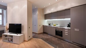 Una cucina moderna con mobili grigi, forno integrato e TV su un mobile bianco.