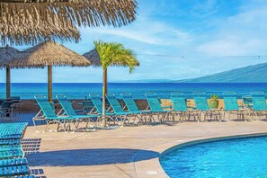 A poolside area with lounge chairs, a palm tree, and a view of the ocean.
