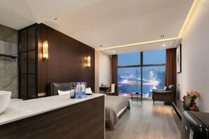 Une chambre d’hôtel moderne dotée d’un grand lit, d’un coin salon, d’un bureau, d’une vue sur la ville et d’une salle de bain.