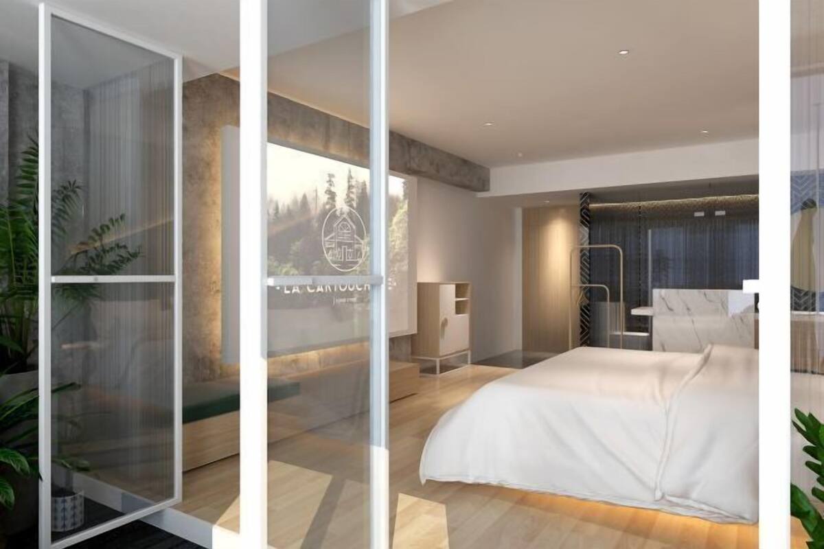Ein modernes Hotelzimmer mit einem großen Bett, einer Glastrennwand und Blick auf eine gebirgige Landschaft.