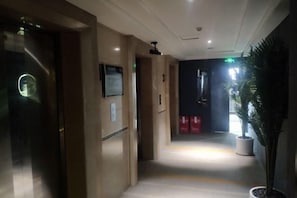 Un couloir d’hôtel avec un comptoir de réception, une plante et un panneau indiquant la direction de l’ascenseur.
