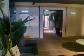 Een hotel lobby met een receptiebalie, een zithoek en een gang die naar andere kamers leidt.