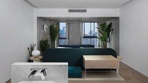 Ein modernes Schlafzimmer mit Bett, kleinem Tisch, Nachttisch und großem Fenster mit Blick auf die Stadt.