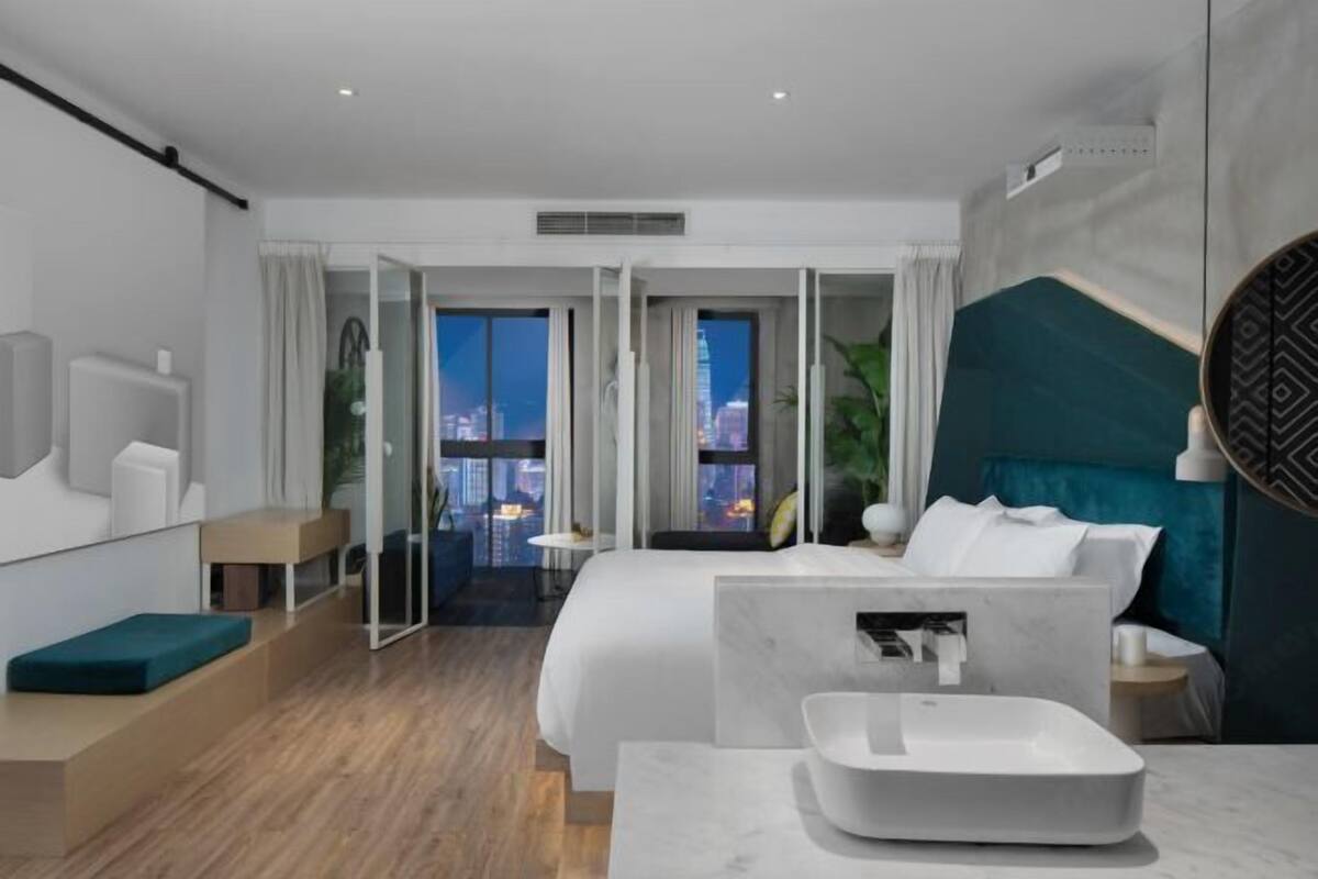 Ein modernes Hotelzimmer mit Bett, Badezimmer, Blick auf die Stadt und einem Balkon.