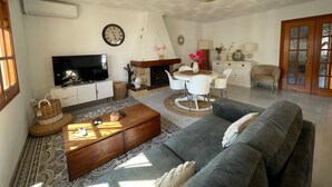 Ett vardagsrum med en soffa, ett soffbord, en tv, en öppen spis, ett matbord, stolar och ett tv-bord.