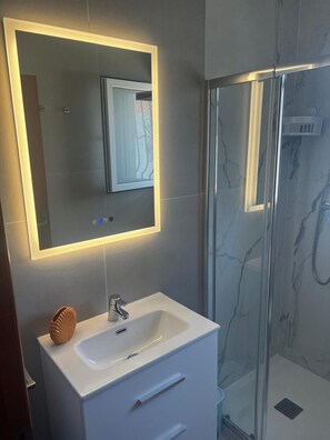 Een moderne badkamer met een grote spiegel, een witte wastafel, een douchecabine van glas en een betegelde wand van marmer.