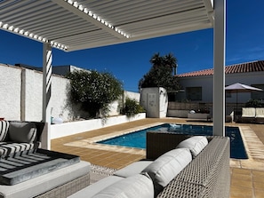 An outdoor pool area with a covered seating area, a small pool, and a white wall.