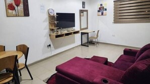 A living room with a TV, a desk, a chair, a sofa, and a dining table with chairs. - Masterpiece 1 bedroom  (Accra)