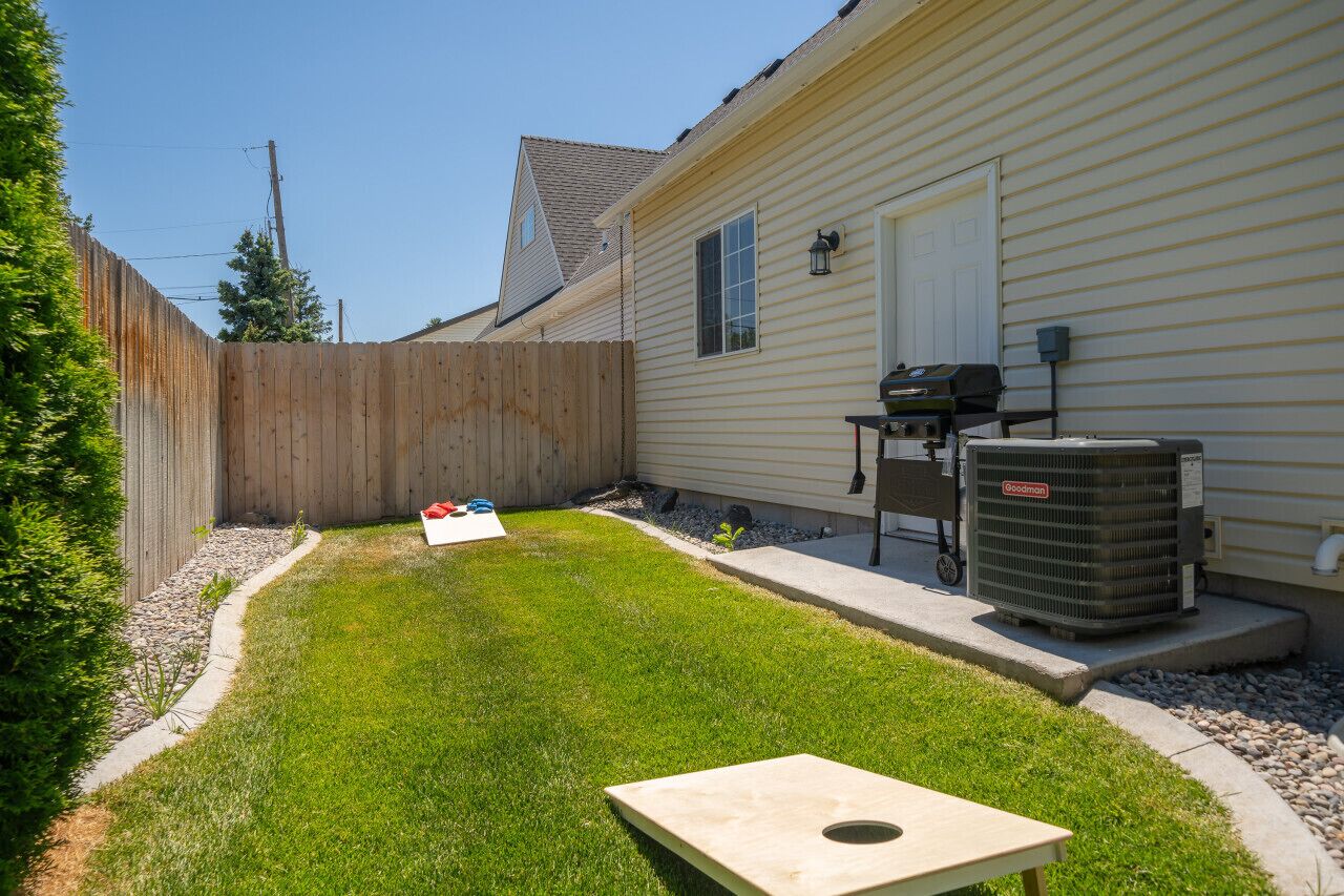 Spacious backyard with a BBQ grill and cornhole game, ideal for outdoor fun and family gatherings.