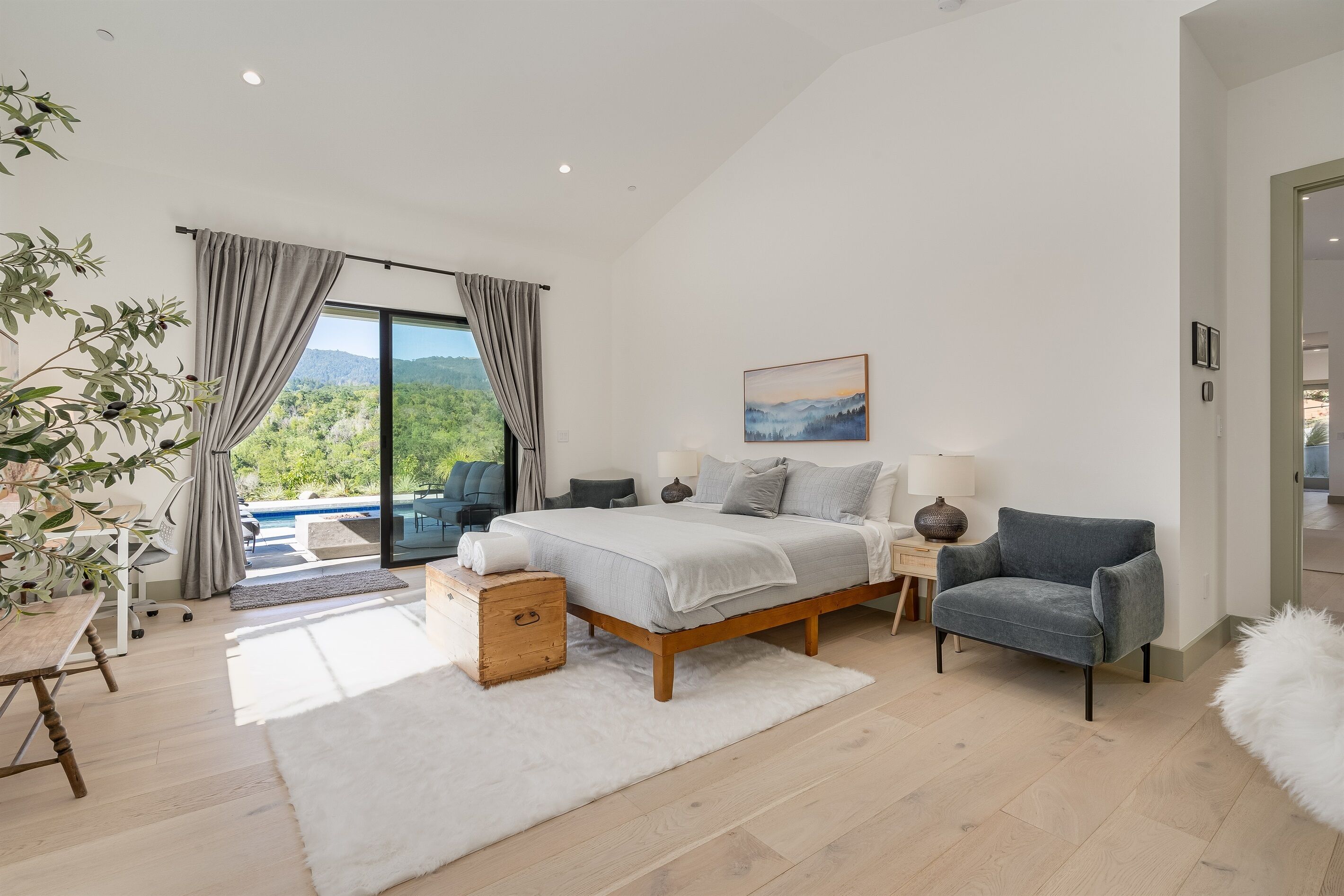 A modern bedroom with a large bed, a view of the outdoors, and a cozy seating area.