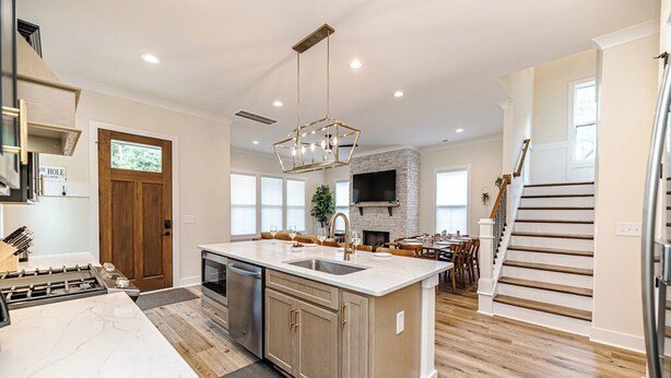 A spacious kitchen with a marble countertop, a central island, and a dining area with wooden flooring and a staircase. - 19th Hole - Pickelball, Park, Walk to Downtown (Southern Pines)
