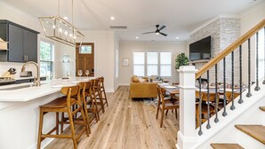 A modern kitchen with a bar area, wooden flooring, and a staircase with a TV mounted on the wall. - 19th Hole - Pickelball, Park, Walk to Downtown (Southern Pines)