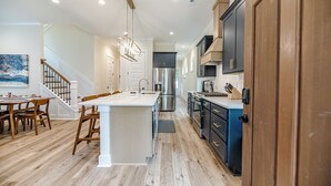 A modern kitchen with a central island, wooden flooring, and built-in appliances. - 19th Hole - Pickelball, Park, Walk to Downtown (Southern Pines)