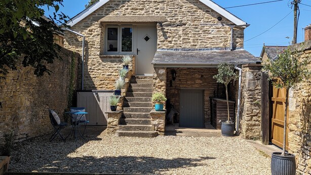 A stone house with a steeply pitched roof, a small front porch, and a gravel driveway. - The Barn, Chipping Norton (Chipping Norton)