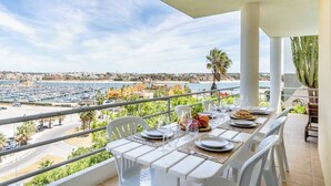 A balcony with a table set for dining, overlooking a marina and beach.