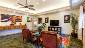A spacious living room with a ceiling fan, a television, and a variety of wall art.