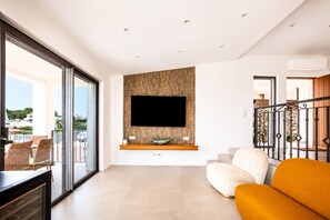 A modern living room with a flat-screen TV mounted on a textured wall, a sofa, and a dining area with wicker chairs.