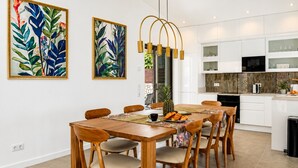A modern kitchen with white cabinets, a central island, and a dining area with a wooden table and chairs. - Villa Oceano by Indigo (Carvoeiro)