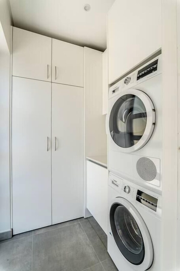 Un cuarto de lavandería con lavadora y secadora de carga frontal, gabinetes blancos y piso de baldosas.