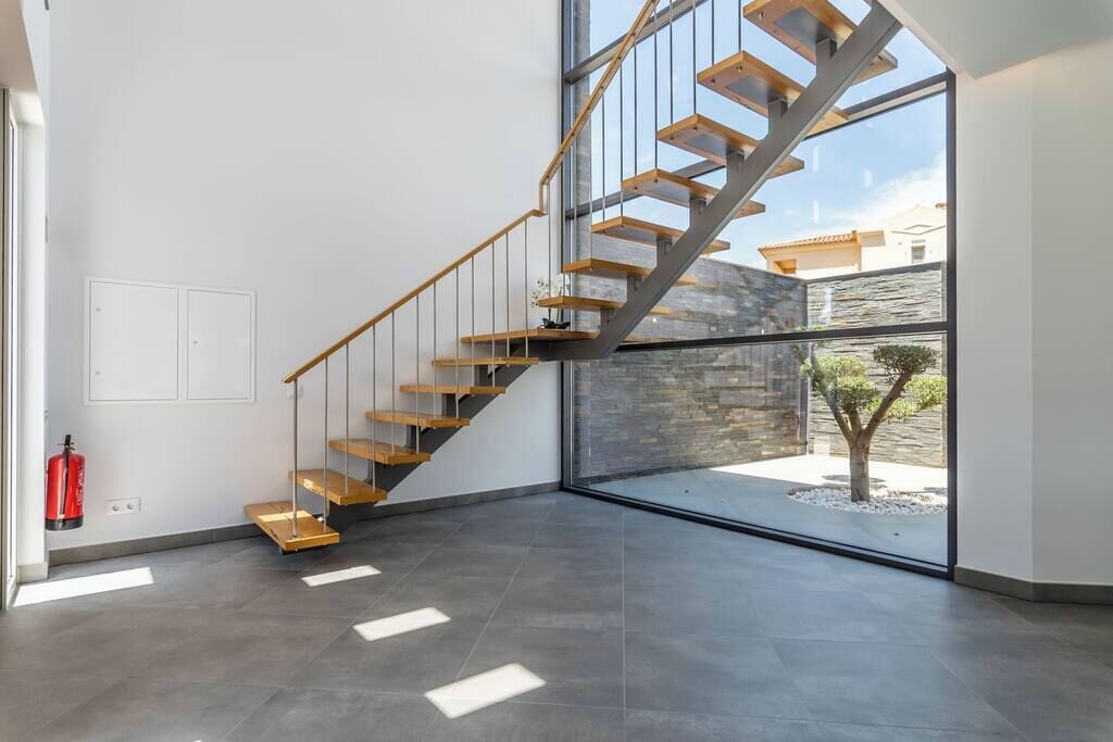 Un intérieur moderne avec un escalier en bois, un mur en pierre et une porte en verre donnant sur l’extérieur.