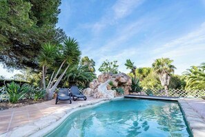 Ein Swimmingpool mit Wasserfall, umgeben von Palmen und einer Steinmauer.
