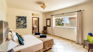 A hotel room with a bed, a chair, a window with curtains, a ceiling fan, and artwork on the wall. - Villa Concha by Indigo (Carvoeiro)
