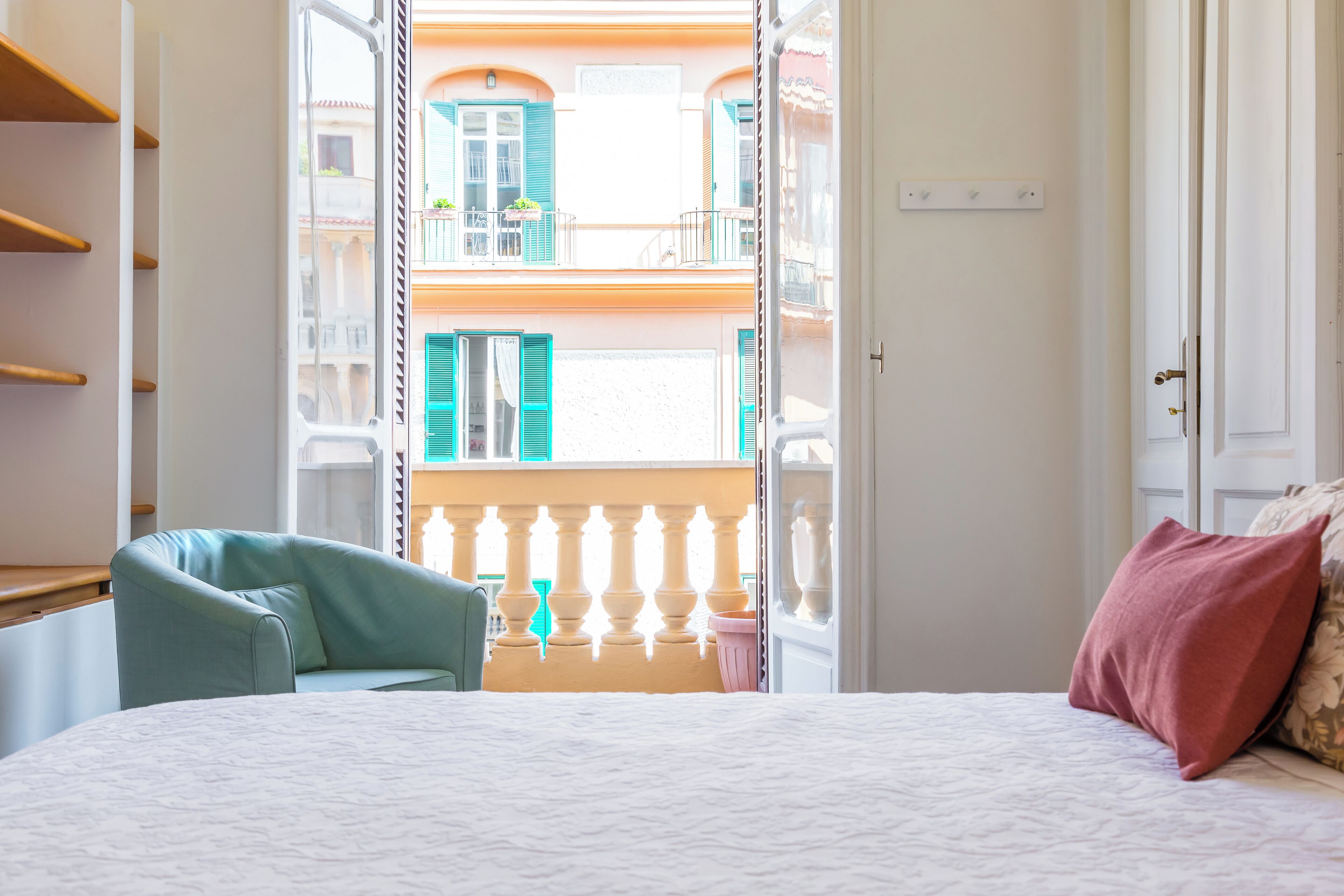 A bedroom with a bed, a chair, and a view of a balcony with a railing.