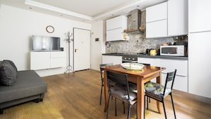 A modern kitchen with white cabinets, a microwave, and a stove. There is a dining table with chairs and a gray sofa in the living area.