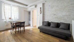 A modern living room with a grey sofa, wooden flooring, and a white brick wall.