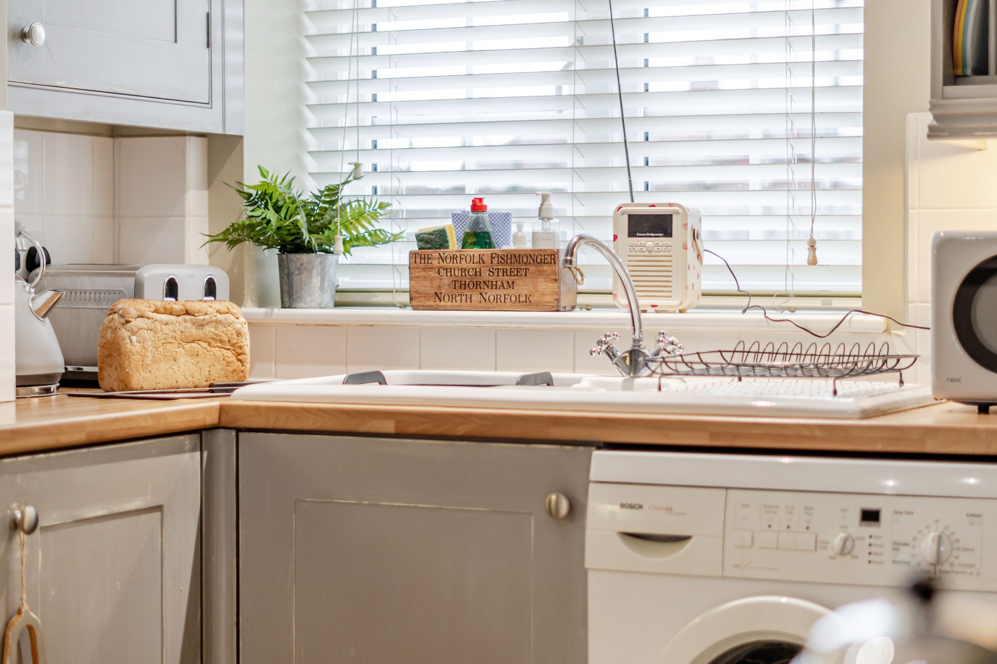 A kitchen with a Bosch dishwasher, a bread loaf, a plant, and a sign for The Norfolk Fishmonger's Church Street Thornham, North Norfolk.