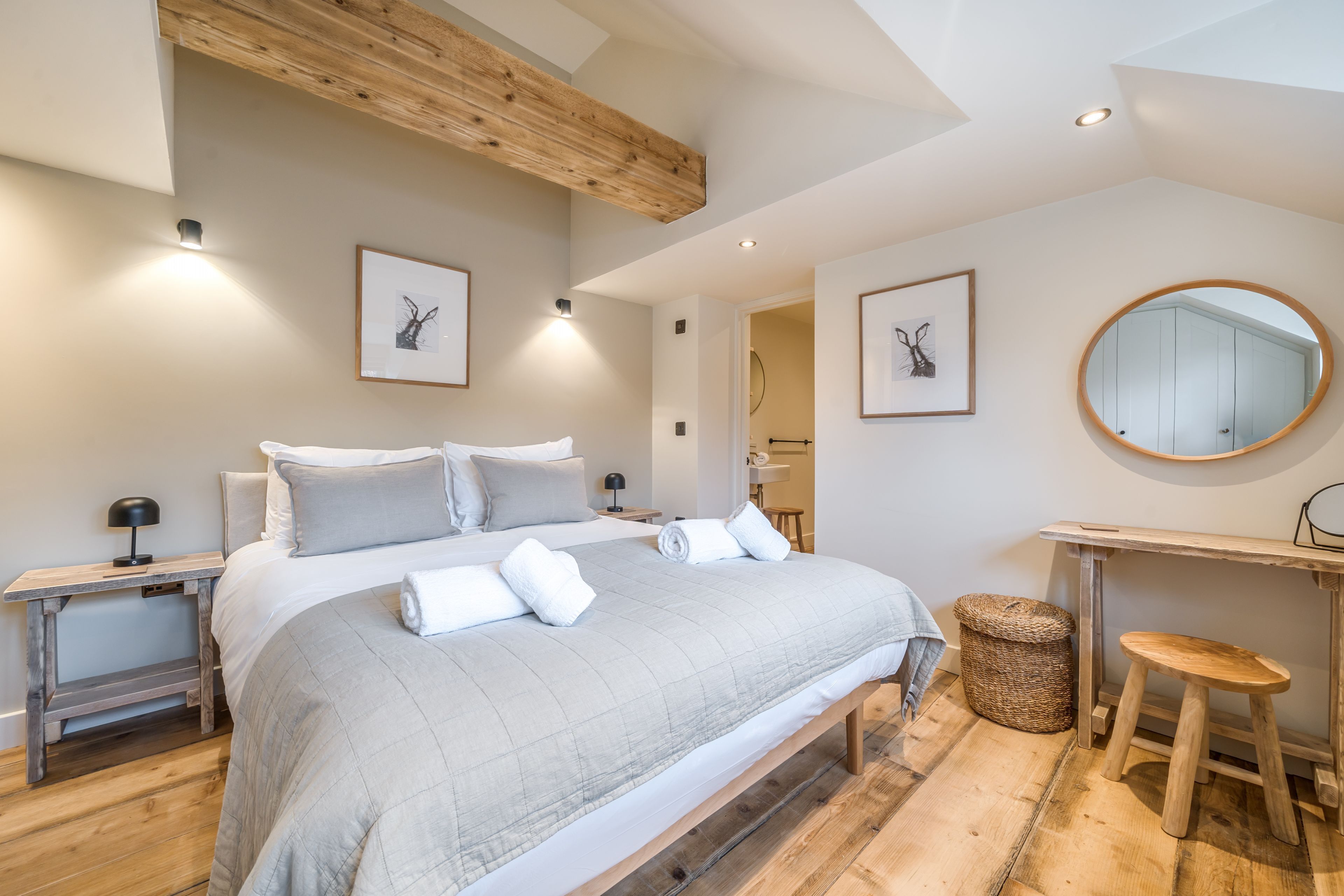 Une chambre moderne avec un grand lit, des poutres en bois, un grand miroir rond et des œuvres d’art encadrées accrochées aux murs.