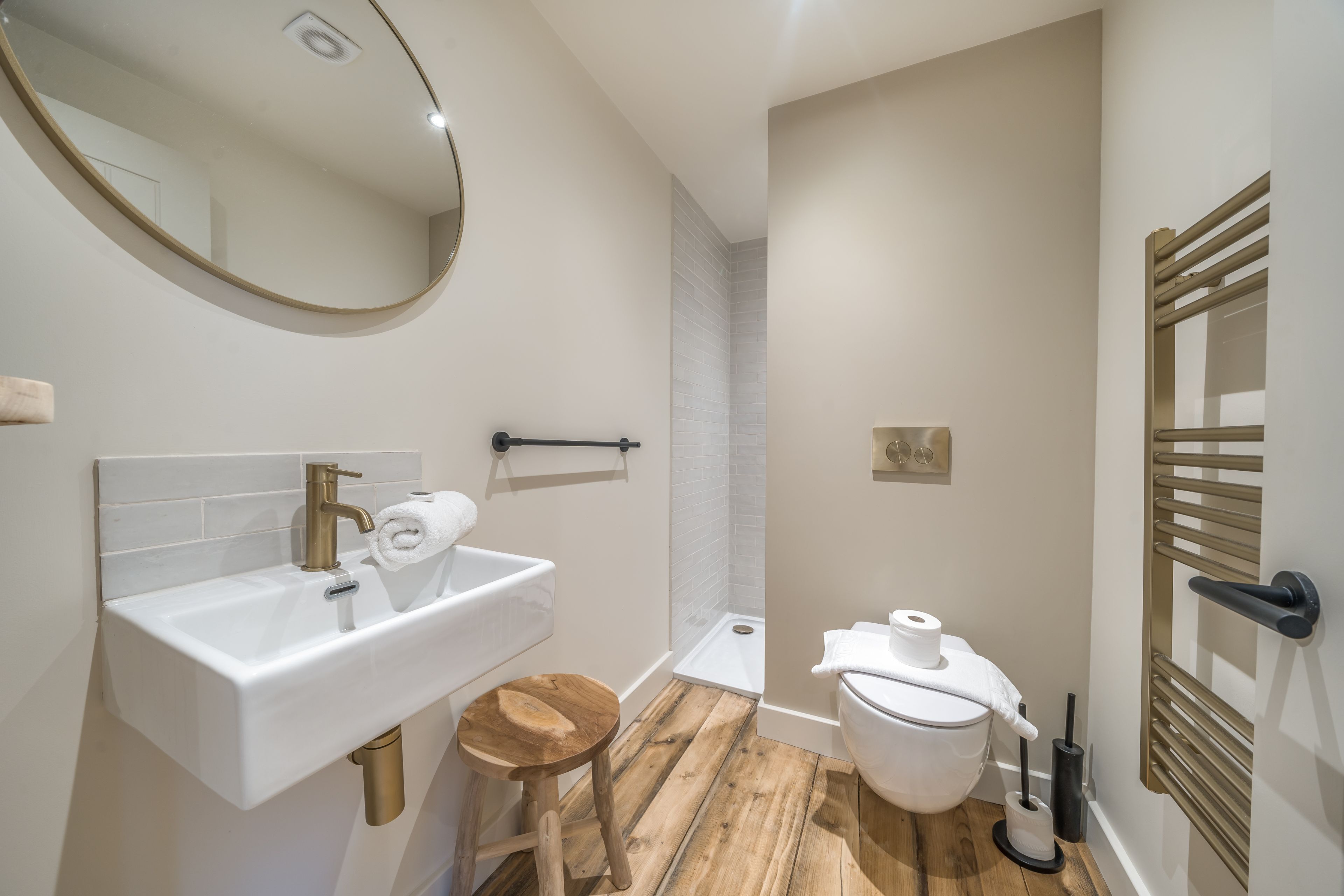A modern bathroom with a white sink, wooden stool, toilet, and a towel rack.