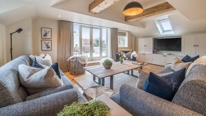 A spacious living room with a large sofa set, a wooden coffee table, and a TV in a white cabinet. - Burnham Loft - sleeps 4 guests  in 2 bedrooms (Burnham Market)