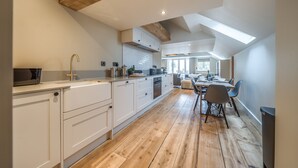 A modern kitchen with wooden beams, white cabinetry, and a dining area with chairs and a table. - Burnham Loft - sleeps 4 guests  in 2 bedrooms (Burnham Market)