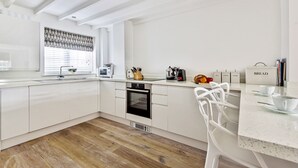 Una cocina moderna con armarios blancos, horno empotrado y una ventana con persianas decorativas.