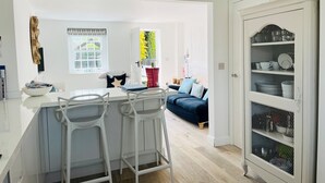 Una cocina moderna con taburetes blancos, una mesa de comedor y un sofá en la sala.