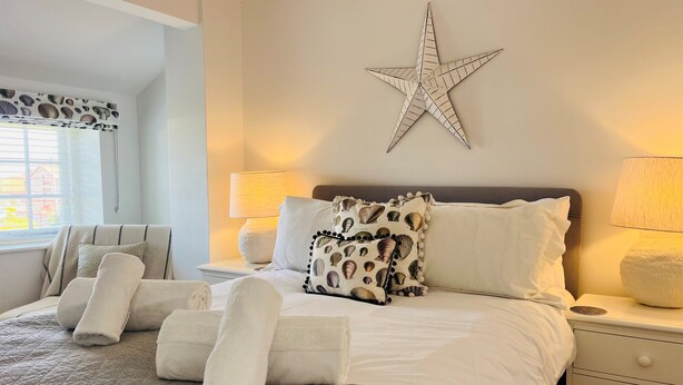 Una cama bien hecha con sábanas blancas, una decoración de estrella en la pared y una ventana con cortinas.