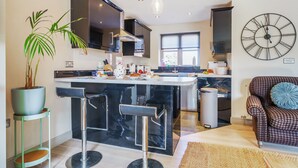 Une cuisine moderne avec un îlot central, des tabourets de bar, une plante en pot et une grande horloge murale.
