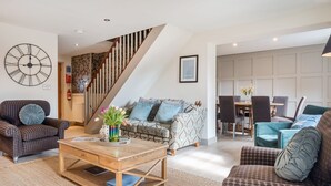 Un salon moderne avec un escalier, des canapés à motifs à carreaux, une table basse en bois et une grande horloge murale.