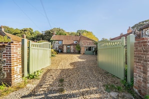 A gravel driveway leading to a house with a brick facade and a tiled roof.