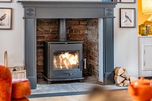 A wood-burning stove in a fireplace with a brick wall, a mantelpiece, and framed pictures on the wall. - Cherryhill - sleeps 5 guests  in 3 bedrooms (North Creake)
