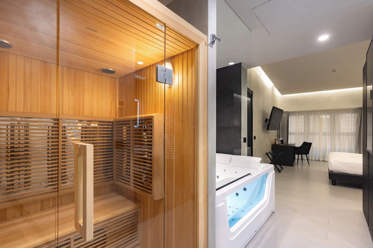 Habitación de hotel moderna con sauna de madera, una bañera grande, un escritorio y una cama.